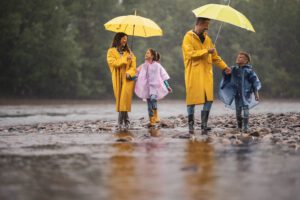 Familia de dos adultos con dos niños paseando por la playa con chubasquero y paraguas.